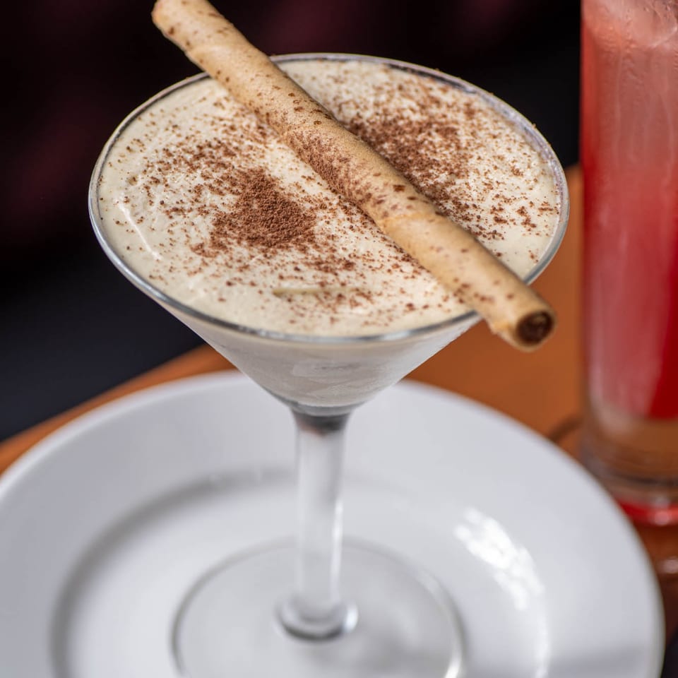 Creamy dessert in a martini glass, topped with cocoa powder and a wafer stick, on a white plate.