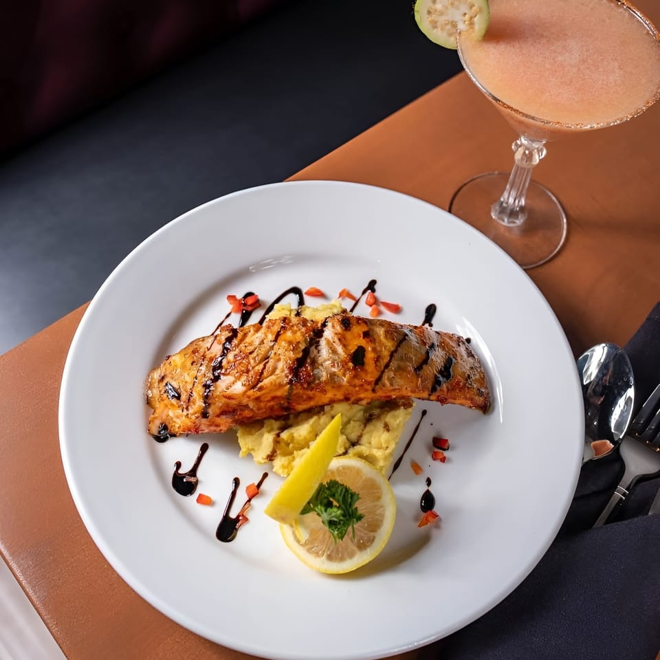 Grilled salmon with mashed potatoes, lemon, and a cocktail with guava garnish.