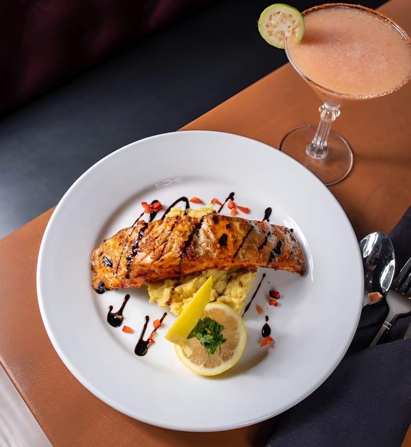 Grilled salmon with mashed potatoes, lemon, and a cocktail with guava garnish.