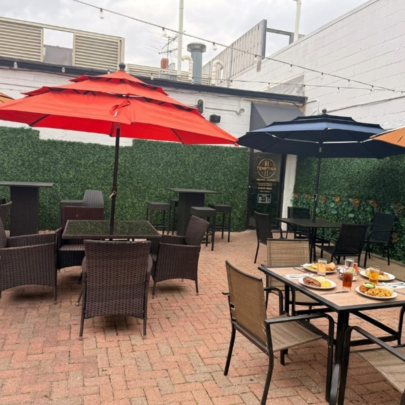 Outdoor patio with red and blue umbrellas, wicker chairs, and food on a table.