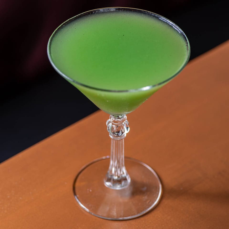 Bright green cocktail in a martini glass on a wooden table.