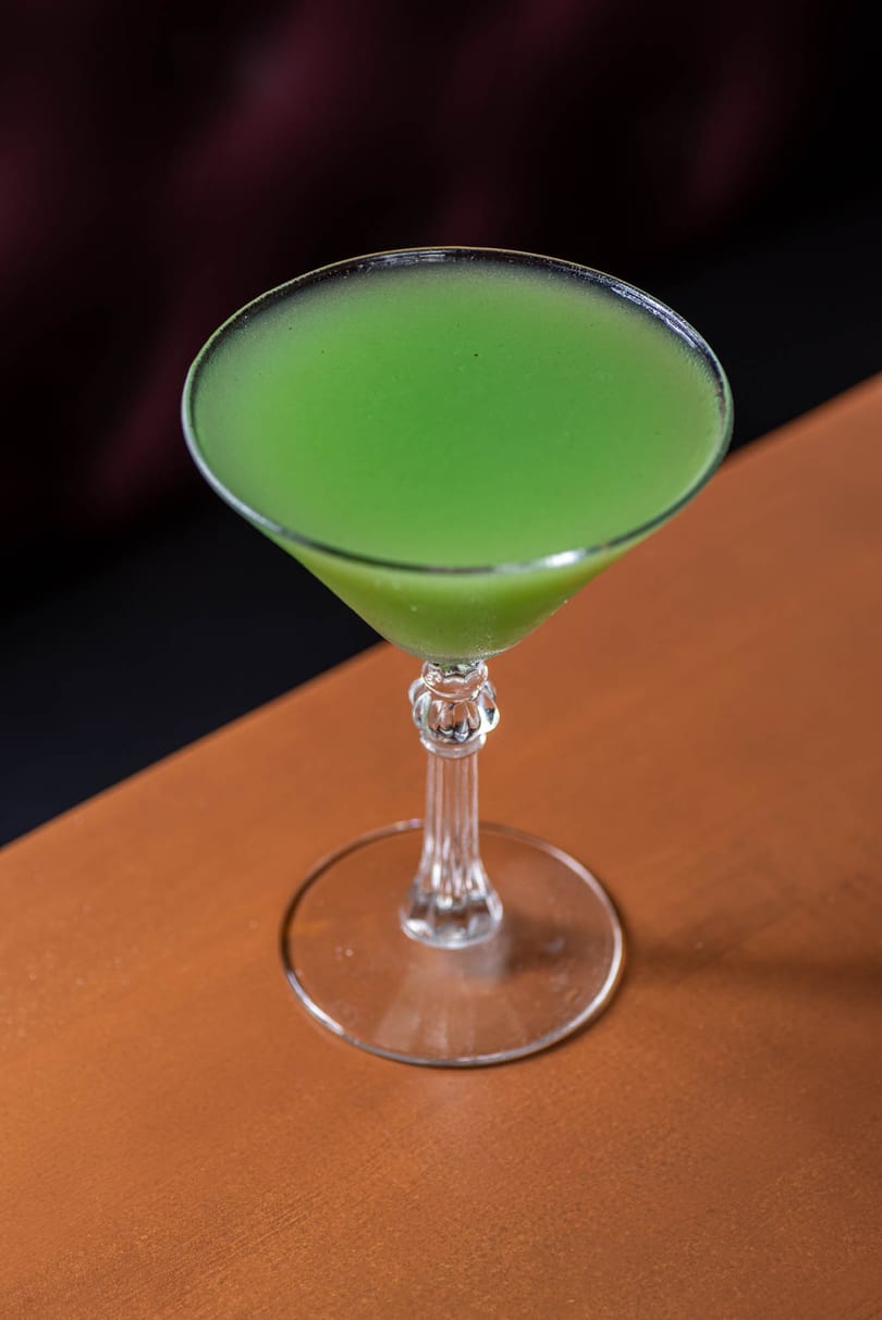 Bright green cocktail in a martini glass on a wooden table.