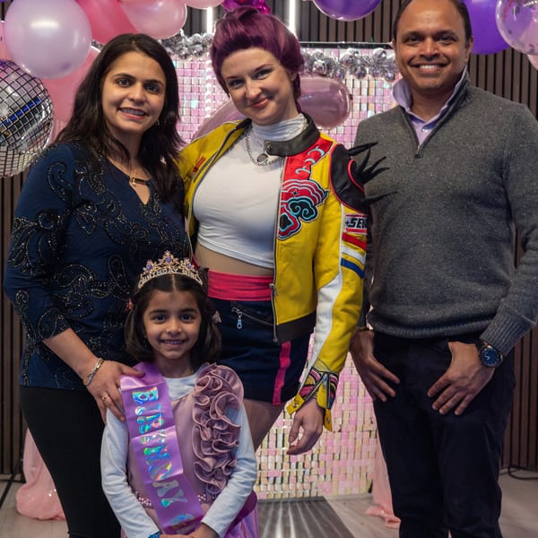Two women, a man, and a young girl in a crown and birthday sash pose with balloons.