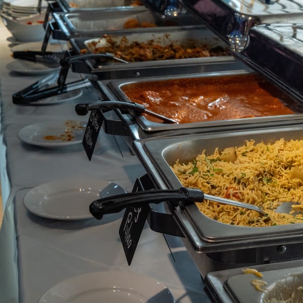 A restaurant buffet line displaying Butter Chicken, Pulao, and other hot food in chafing dishes.