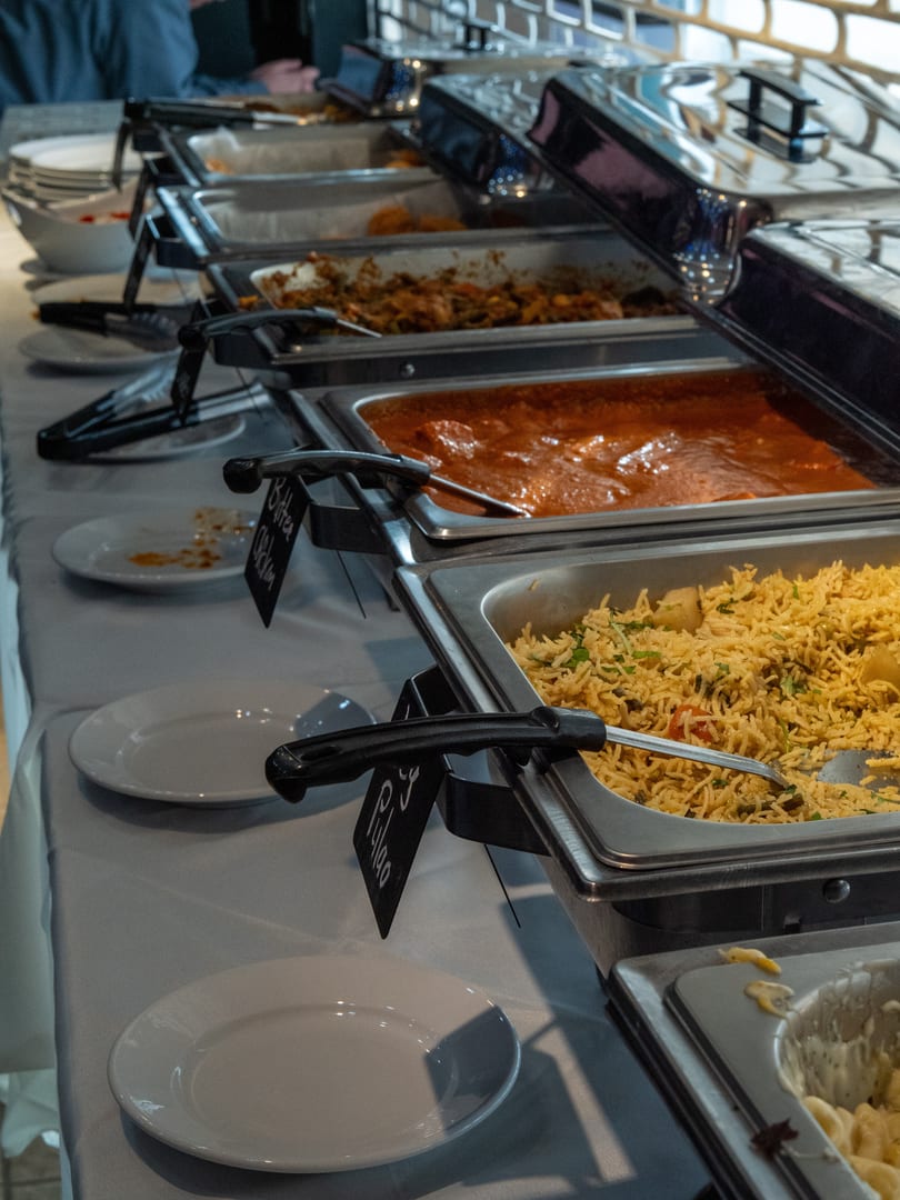 A restaurant buffet line displaying Butter Chicken, Pulao, and other hot food in chafing dishes.