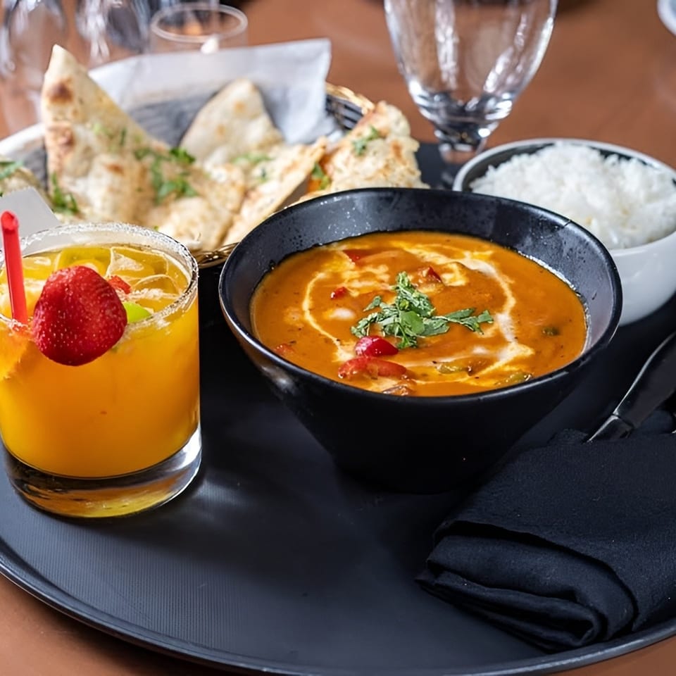Indian meal with curry, rice, naan bread, and a mango drink with a strawberry garnish.