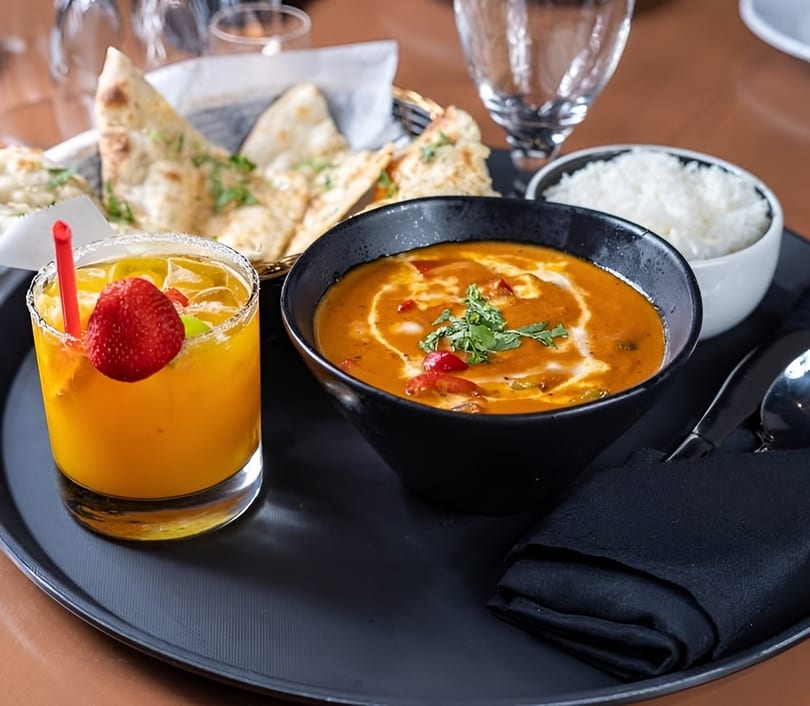 Indian meal with curry, rice, naan bread, and a mango drink with a strawberry garnish.