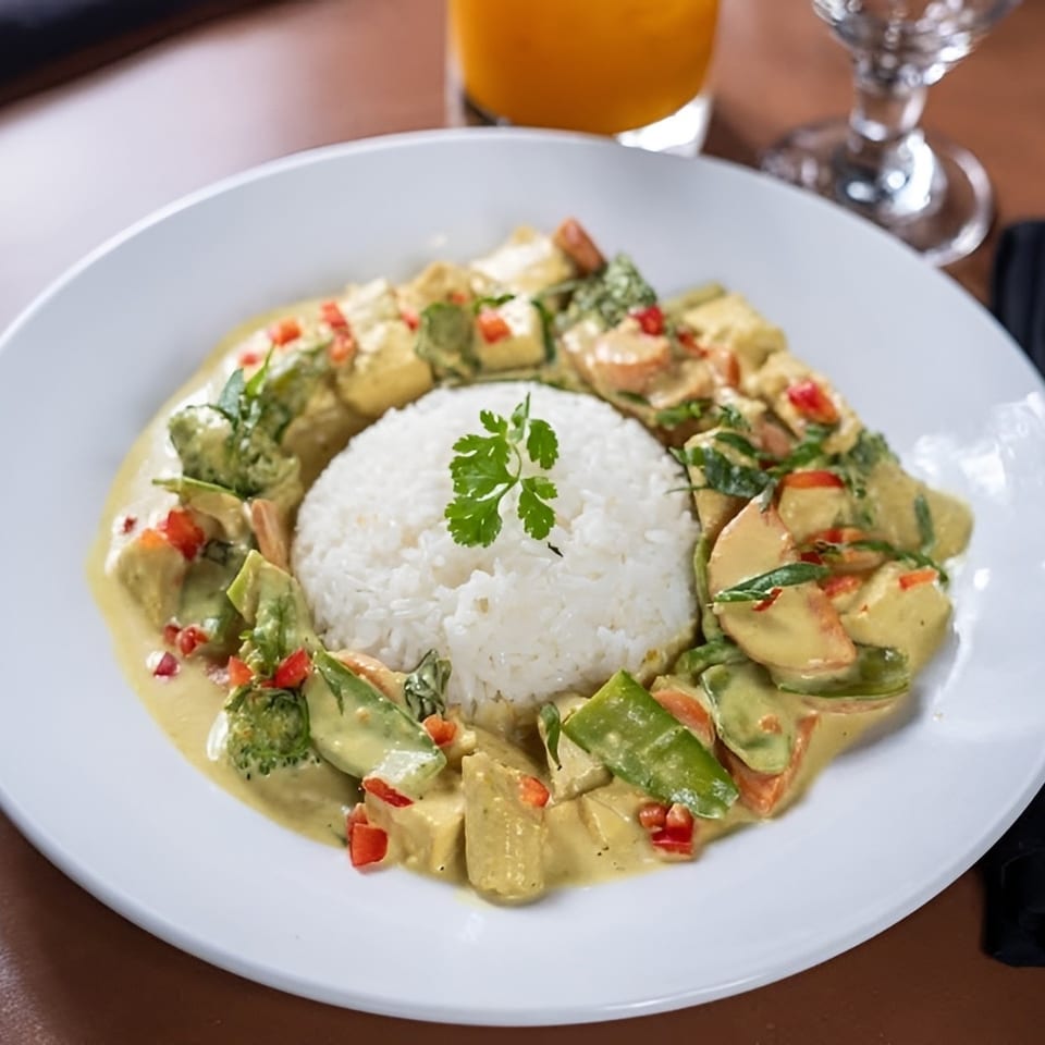 A white plate with a mound of white rice surrounded by yellow curry with vegetables and tofu.